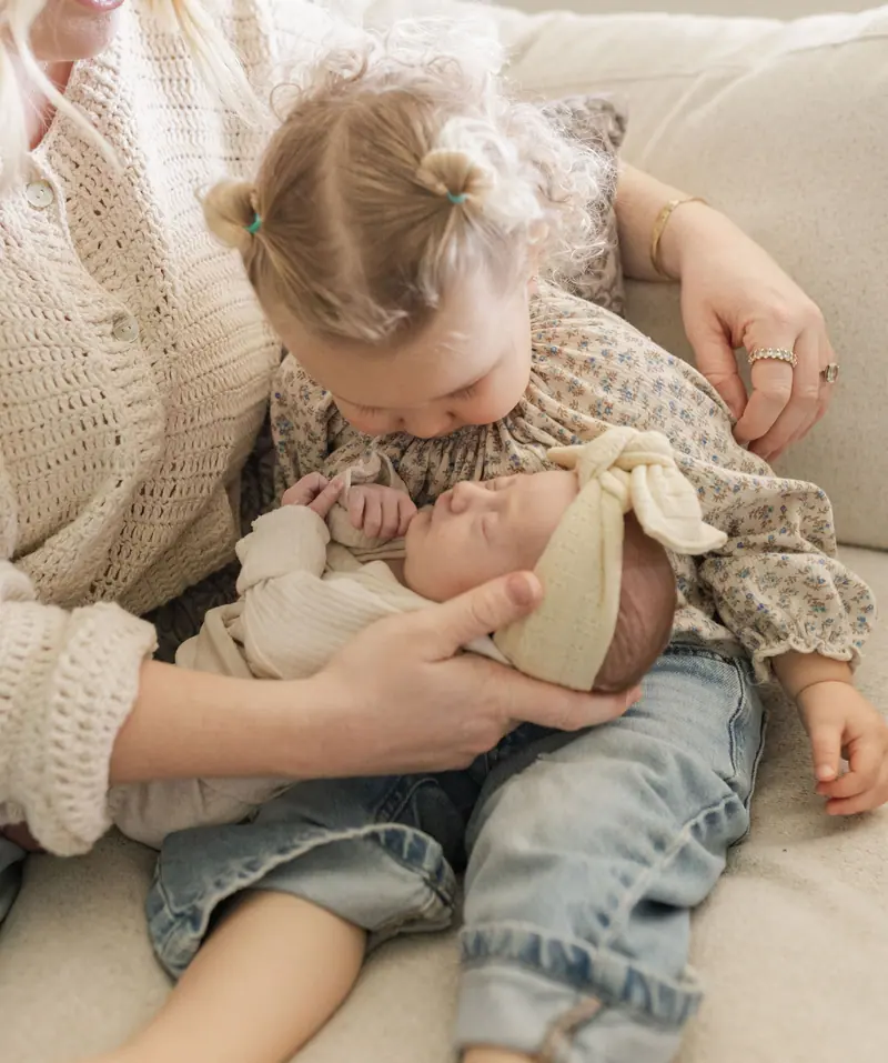 A toddler kissing her newborn sibling's head on the couch