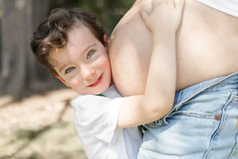 A son resting his cheek against his mom's belly