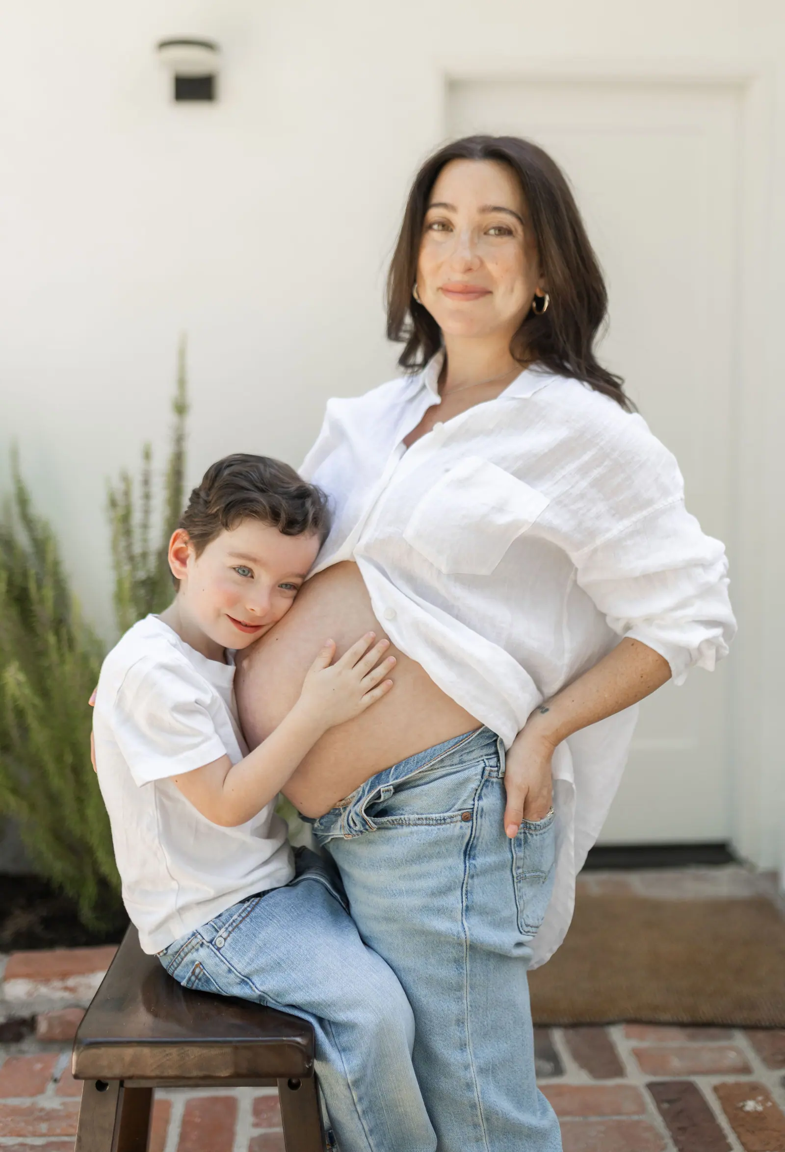 A young boy hugging his pregnant mother's belly while she smiles