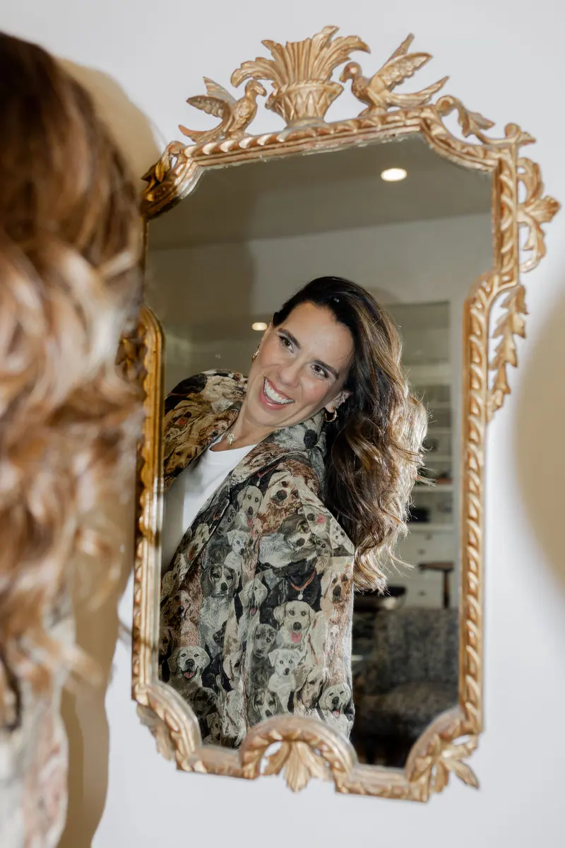 A woman smiling at her reflection in an ornate gold mirror