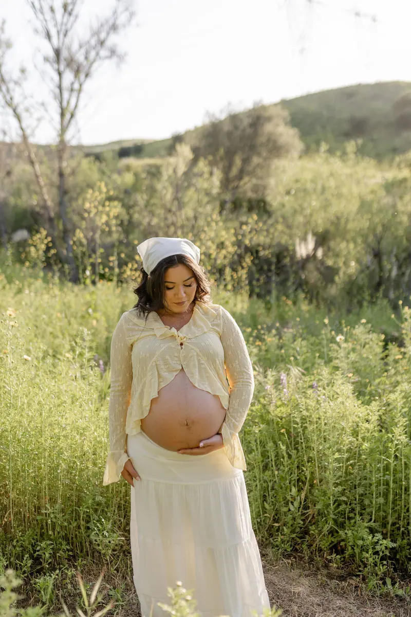 An expecting mother in cream cradling her belly in a green field
