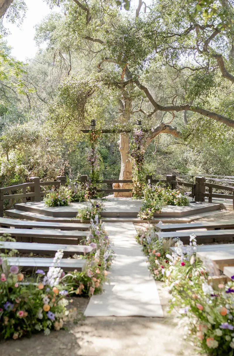 A wildflower-lined aisle and empty benches under a sprawling oak