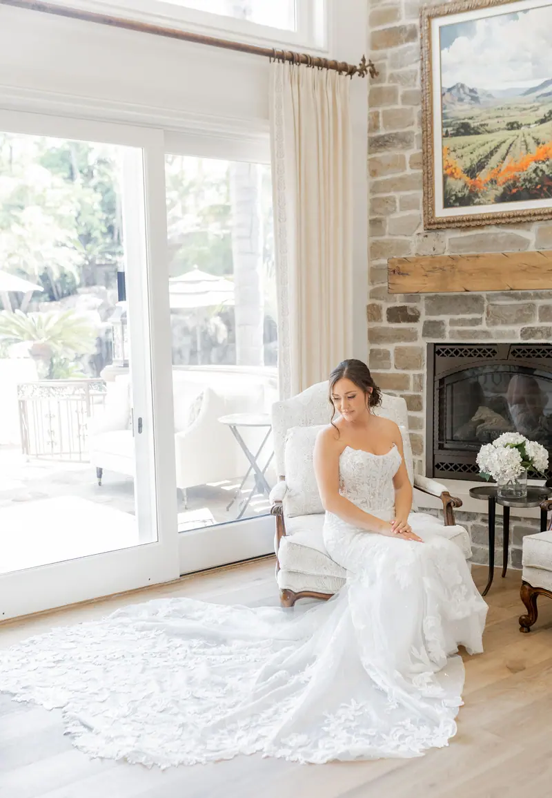 A bride seated by a window with her lace train spread across the floor
