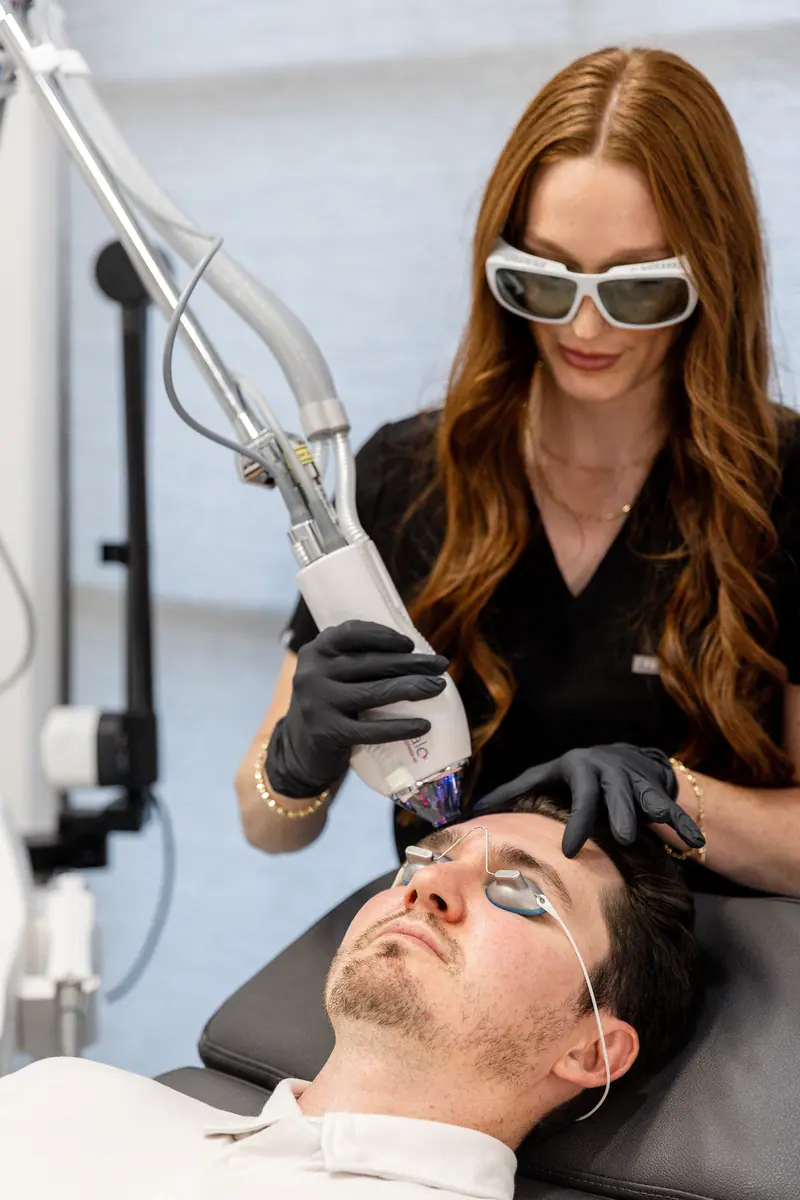 An aesthetician in laser goggles running a treatment on a client's face
